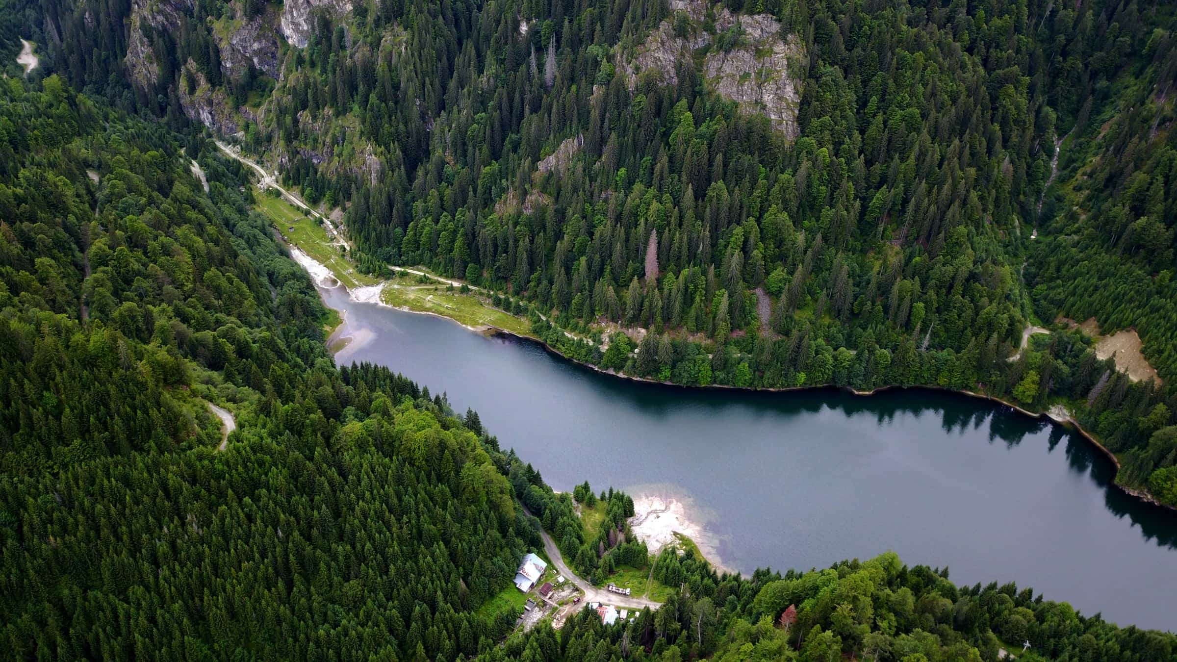 Aerial view of a reservoir cradled by steep, forested mountainsides near Voineasa.